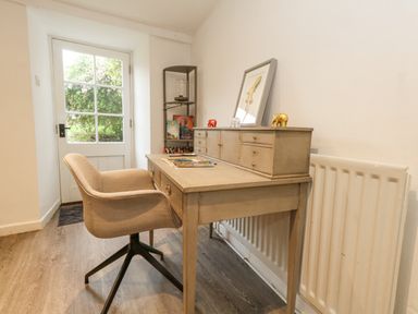 A desk with small drawers and decorative elephants next to a beige chair in a room with a glass door at Half Pint Cottage in Beaminster