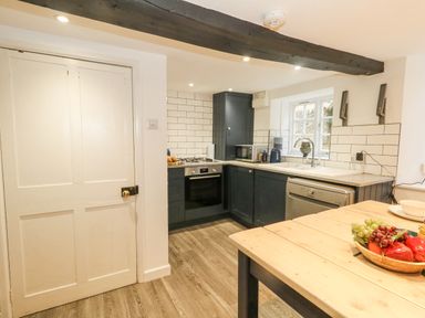 A kitchen with dark cabinets wooden table fruit bowl and a white door at Half Pint Cottage in Beaminster