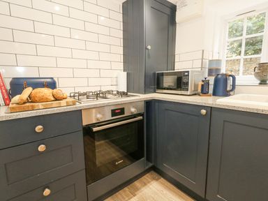 A kitchen corner with a gas stove oven microwave kettle and bread on a cutting board at Half Pint Cottage in Beaminster