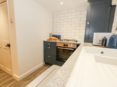 A kitchen with a gas stove and oven dark cabinets a countertop with bread a microwave and a sink at Half Pint Cottage in Beaminster