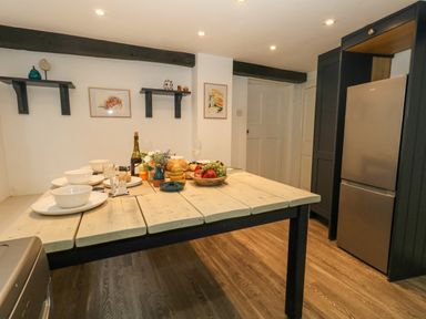 A kitchen with a wooden dining table set with dishes glasses and fruit next to a stainless steel refrigerator at Half Pint Cottage Beaminster
