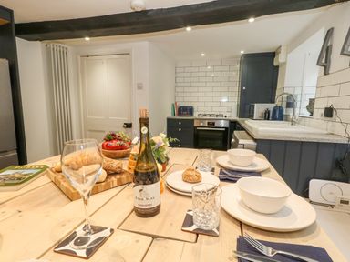 A kitchen with a wooden table set for two with plates glasses bread and a bottle of wine at Half Pint Cottage in Beaminster