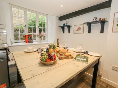 A dining area with a wooden table set with plates bowls glasses and a bowl of fruit under a window at Half Pint Cottage in Beaminster