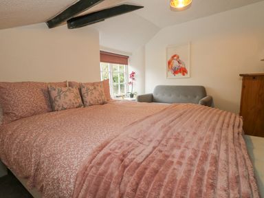 Bedroom with pink bedding a window gray sofa and wooden dresser at Half Pint Cottage in Beaminster