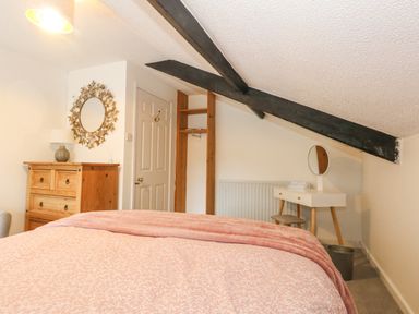 A bedroom with a bed covered with a pink blanket wooden chest of drawers and a dressing table with a round mirror at Half Pint Cottage in Beaminster