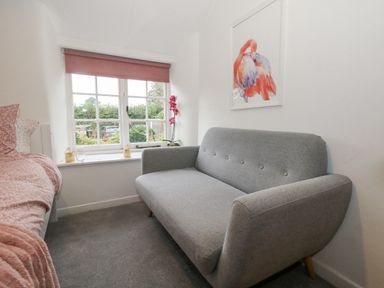 A small room with a gray sofa a bed with pink bedding a window with a pink blind and a framed flamingo picture on the wall at Half Pint Cottage Beaminster