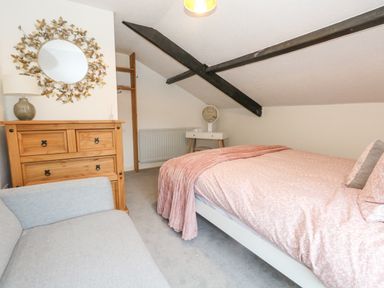 A bedroom with a bed covered with pink bedding a wooden dresser a round mirror and a gray sofa at Half Pint Cottage in Beaminster