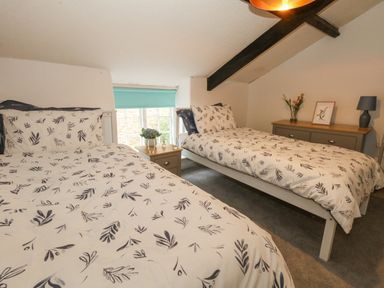 A bedroom with two beds a window with a blue blind and a dresser with flowers at Half Pint Cottage in Beaminster