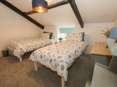 A bedroom with two single beds a desk a small window and wooden beams on the ceiling at Half Pint Cottage in Beaminster