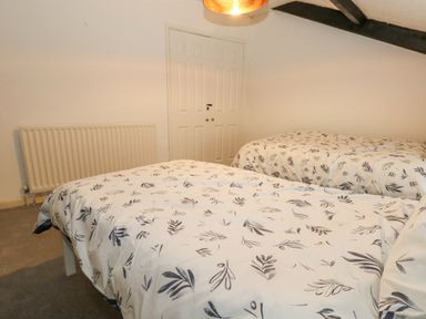 A bedroom with two beds a radiator a door and ceiling beams at Half Pint Cottage Beaminster