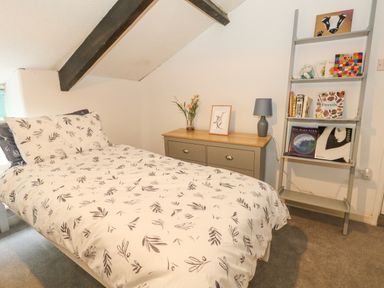 A bedroom with a single bed a chest of drawers with a lamp and flowers and a ladder shelf with books at Half Pint Cottage in Beaminster