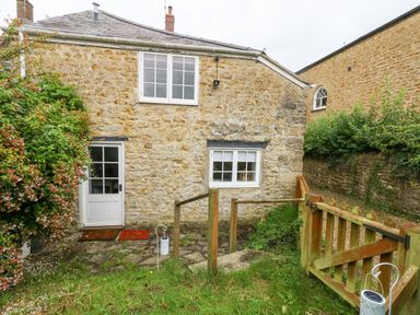 A stone cottage with white framed windows and a door with a garden gate and greenery at Half Pint Cottage in Beaminster