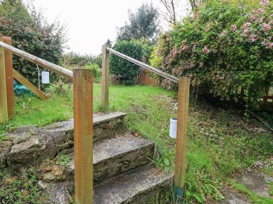 Outdoor stone steps with wooden handrails and hanging lanterns leading to a grassy area with bushes at Half Pint Cottage in Beaminster