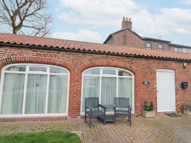 Exterior of a brick cottage with two large arched windows a white door two outdoor chairs and plants at Fulmar Cottage in Flamborough