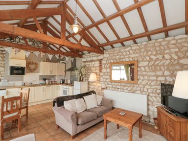 A living area with kitchen cabinets dining table sofa coffee table television and stone walls at Fulmar Cottage in Flamborough