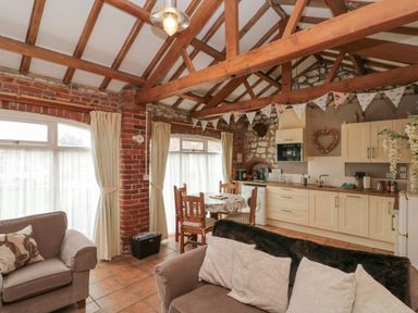 An open plan living area with beige sofas a small dining table wooden chairs and a kitchen with cream cupboards under exposed wooden beams at Fulmar Cottage in Flamborough
