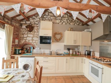 A kitchen with cream cabinets wooden countertops a washing machine a dining table and chairs stone and brick walls at Fulmar Cottage in Flamborough