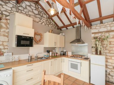 A kitchen with cream cabinets a gas stove a microwave a refrigerator and exposed wooden beams at Fulmar Cottage in Flamborough