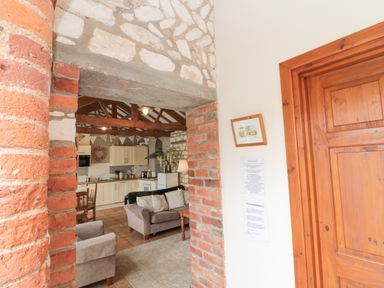 A living room and kitchen area with wooden beams stone and brick walls and wooden door at Fulmar Cottage in Flamborough