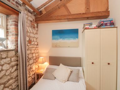 A bedroom with a bed with pillows a bedside table with a lamp a wardrobe with board games on top and stone walls at Fulmar Cottage in Flamborough