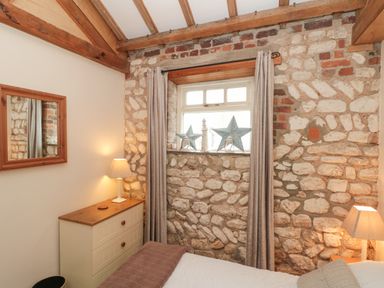 A bedroom with exposed stone walls a dresser with a lamp a window with curtains and star decorations at Fulmar Cottage in Flamborough