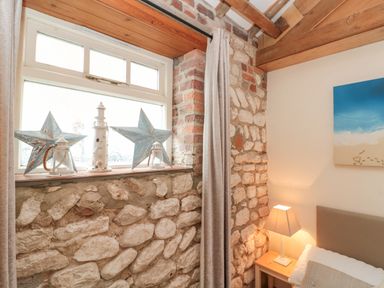 A bedroom corner with stone walls a window with star and lighthouse decorations and a bedside table with a lamp at Fulmar Cottage in Flamborough