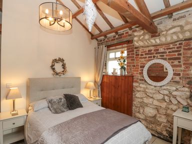 A bedroom with a bed two bedside tables lamps a window and a stone and brick wall at Fulmar Cottage Flamborough