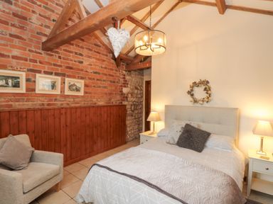 A bedroom with a bed and pillows two bedside tables with lamps a chair and exposed brick and stone walls at Fulmar Cottage in Flamborough