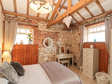 A bedroom with a bed pillows a dresser a vanity table and wooden panel walls at Fulmar Cottage in Flamborough
