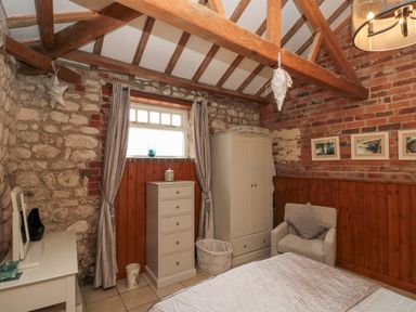 A bedroom with exposed stone and brick walls a window with curtains a chest of drawers a wardrobe an armchair and a bed at Fulmar Cottage in Flamborough