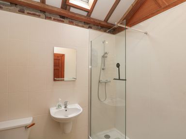 A bathroom with a shower area with glass partition a sink with a mirror and a toilet at Fulmar Cottage in Flamborough