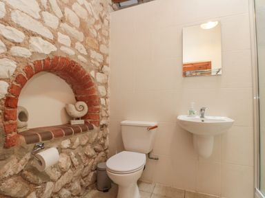 A bathroom with a toilet sink mirror and stone wall with arch at Fulmar Cottage in Flamborough