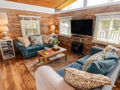 A living room with two blue sofas a wooden coffee table a rug a wall-mounted television and lamps at The Bird House in Cenarth
