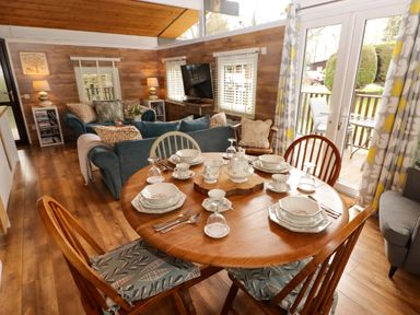 A dining table set with plates cups and cutlery in a living room with sofas a television and glass doors leading to a deck at The Bird House in Cenarth