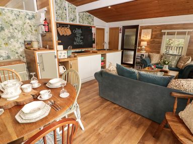 A kitchen and living area with a dining table set with dishes and cups a sofa set with cushions and a coffee table at The Bird House in Cenarth