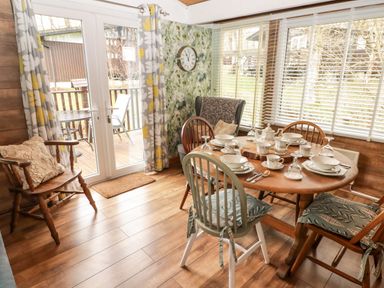 A dining area with a wooden table set with dishes and chairs near large windows and a door leading outside at The Bird House in Cenarth