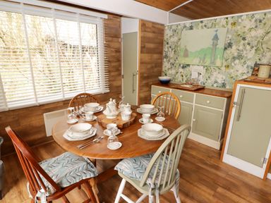 A dining room with a round wooden table set with dishes and cups four chairs and cabinets with floral wallpaper at The Bird House in Cenarth