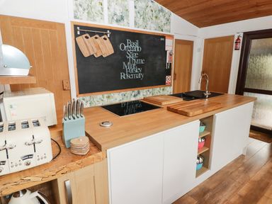 A kitchen countertop with cutting boards knives toaster microwave and a chalkboard with herb names at The Bird House in Cenarth