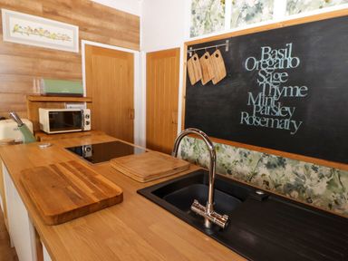 A kitchen counter with wooden cutting boards a sink a blackboard with herbs listed and kitchen appliances at The Bird House in Cenarth
