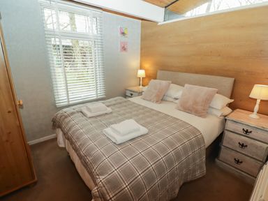 A bedroom with a double bed with pillows and folded towels bedside tables with lamps a wardrobe and a window at The Bird House in Cenarth