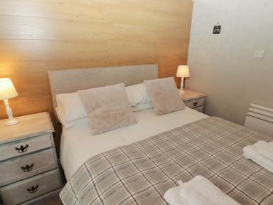 A bedroom with a bed with pillows and a checked blanket and two bedside tables with lamps at The Bird House in Cenarth