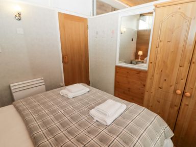 A bedroom with a plaid bedspread and folded towels on the bed next to a wooden wardrobe and door at The Bird House in Cenarth