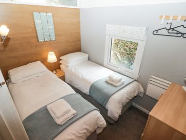 A bedroom with two single beds bedside table and lamp a window with a white blind and hangers on the wall at The Bird House in Cenarth