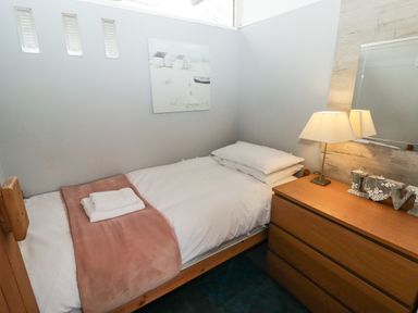 A small bedroom with a single bed towels on the bed and a wooden dresser with a lamp and mirror at The Bird House in Cenarth