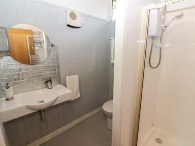 A bathroom with a sink a round mirror a towel rail a toilet and a shower enclosure at The Bird House in Cenarth