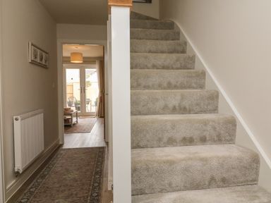 Carpeted staircase next to hallway with radiator rug and artwork leading to room with chairs and table at Seashell Sands in Appledore
