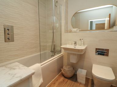 A bathroom with a bathtub shower combination sink with toiletries a toilet and a wicker basket at Seashell Sands in Appledore