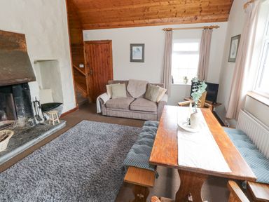 A living room with a fireplace a sofa wooden dining table with benches and windows at Bofin in Oughterard County Galway