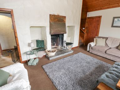 A living room with a fireplace cushions on built in seats sofas and a gray rug at Bofin in Oughterard County Galway