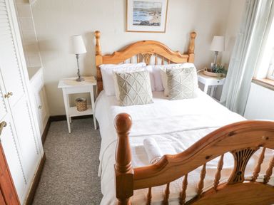 A bedroom with a wooden bed frame two pillows two side tables two lamps and a window with curtains at Bofin in Oughterard County Galway